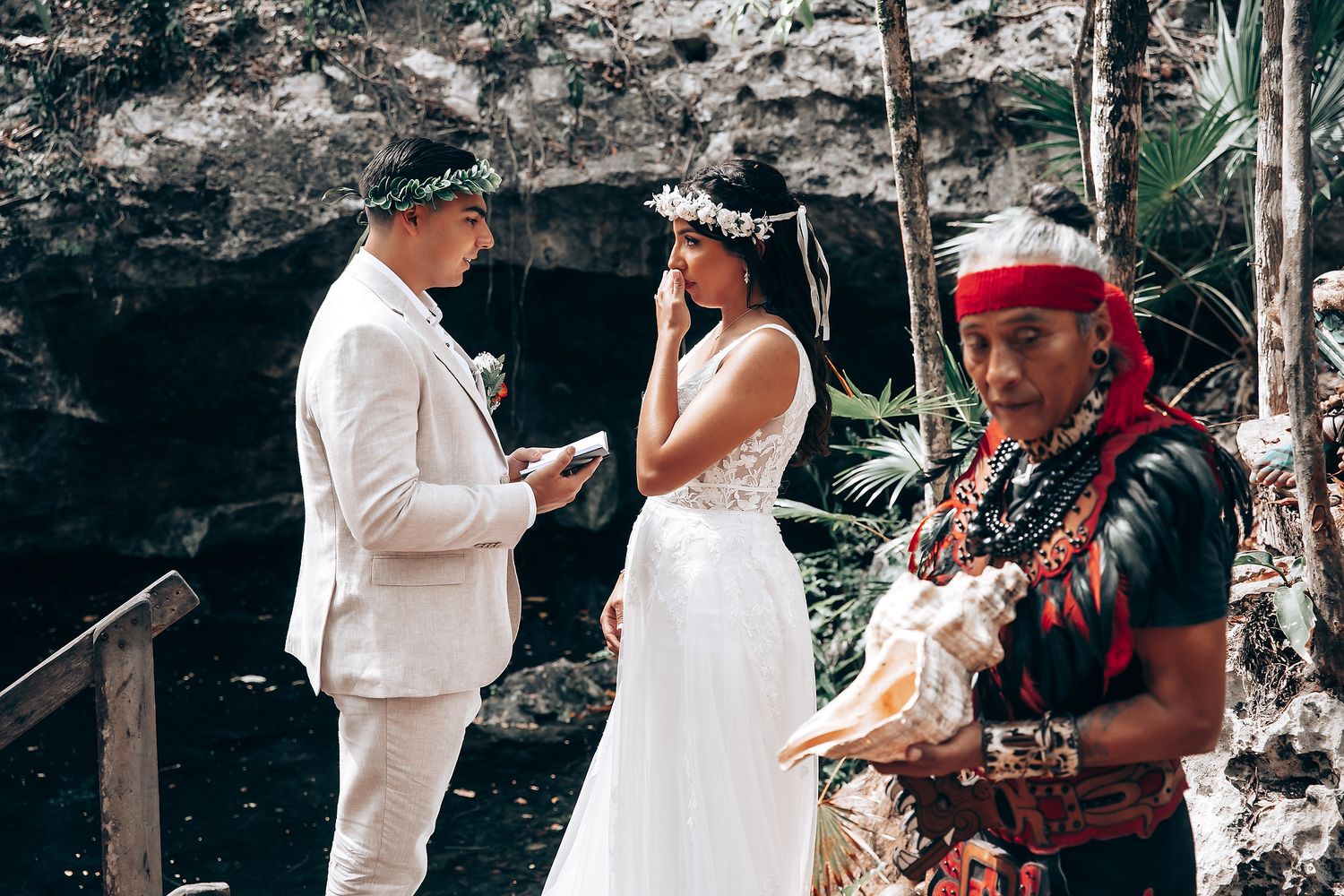 Traditional wedding ceremony taking place in a natural forest setting with attendees in white.