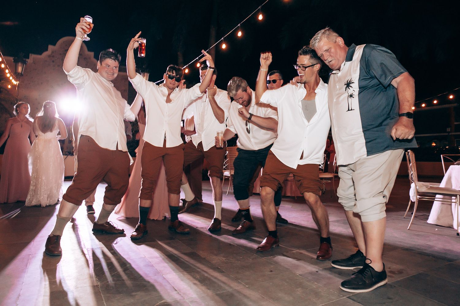 Wedding reception dance floor filled with guests celebrating under string lights.