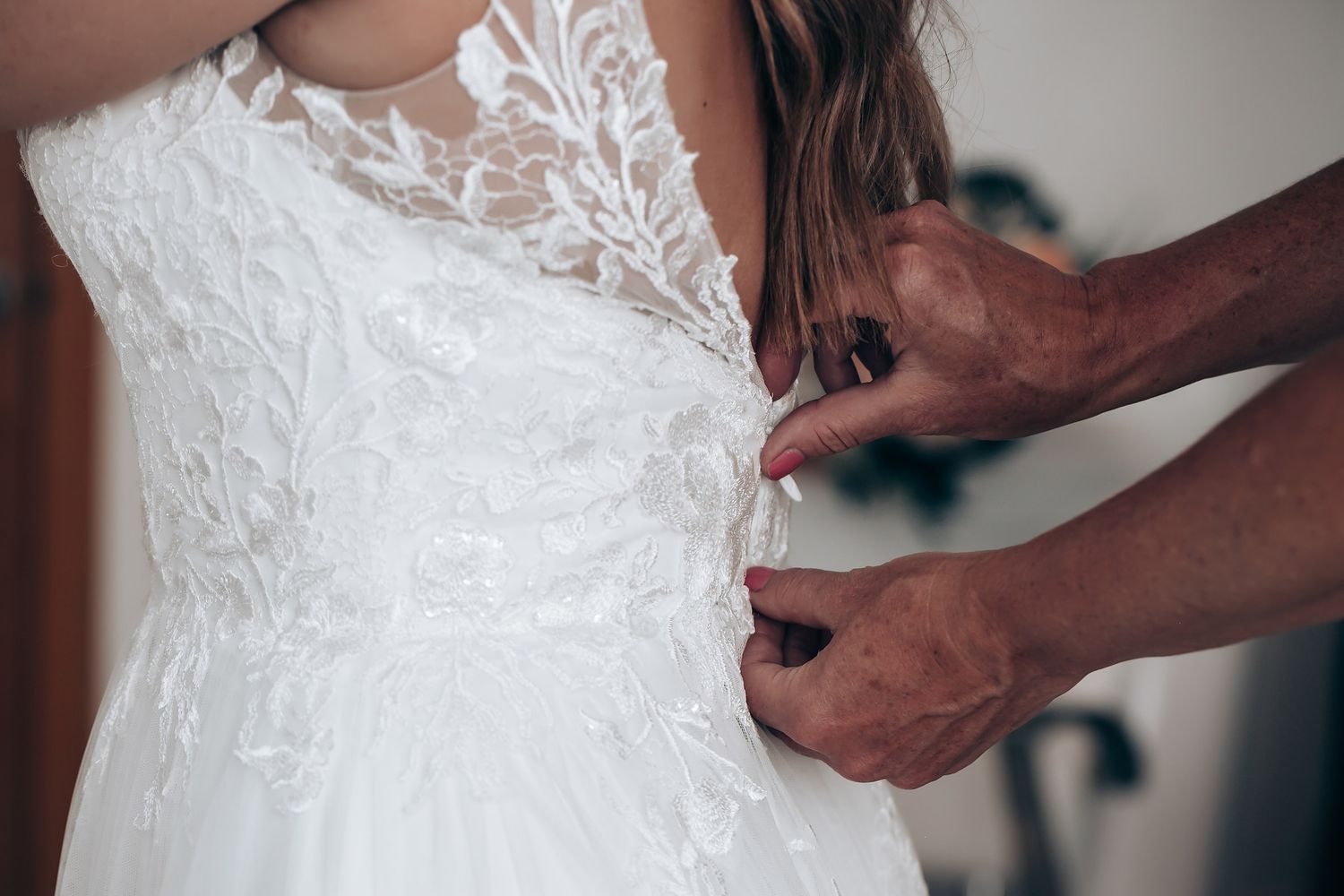 Close-up view of someone adjusting the delicate lace details on a white wedding dress.