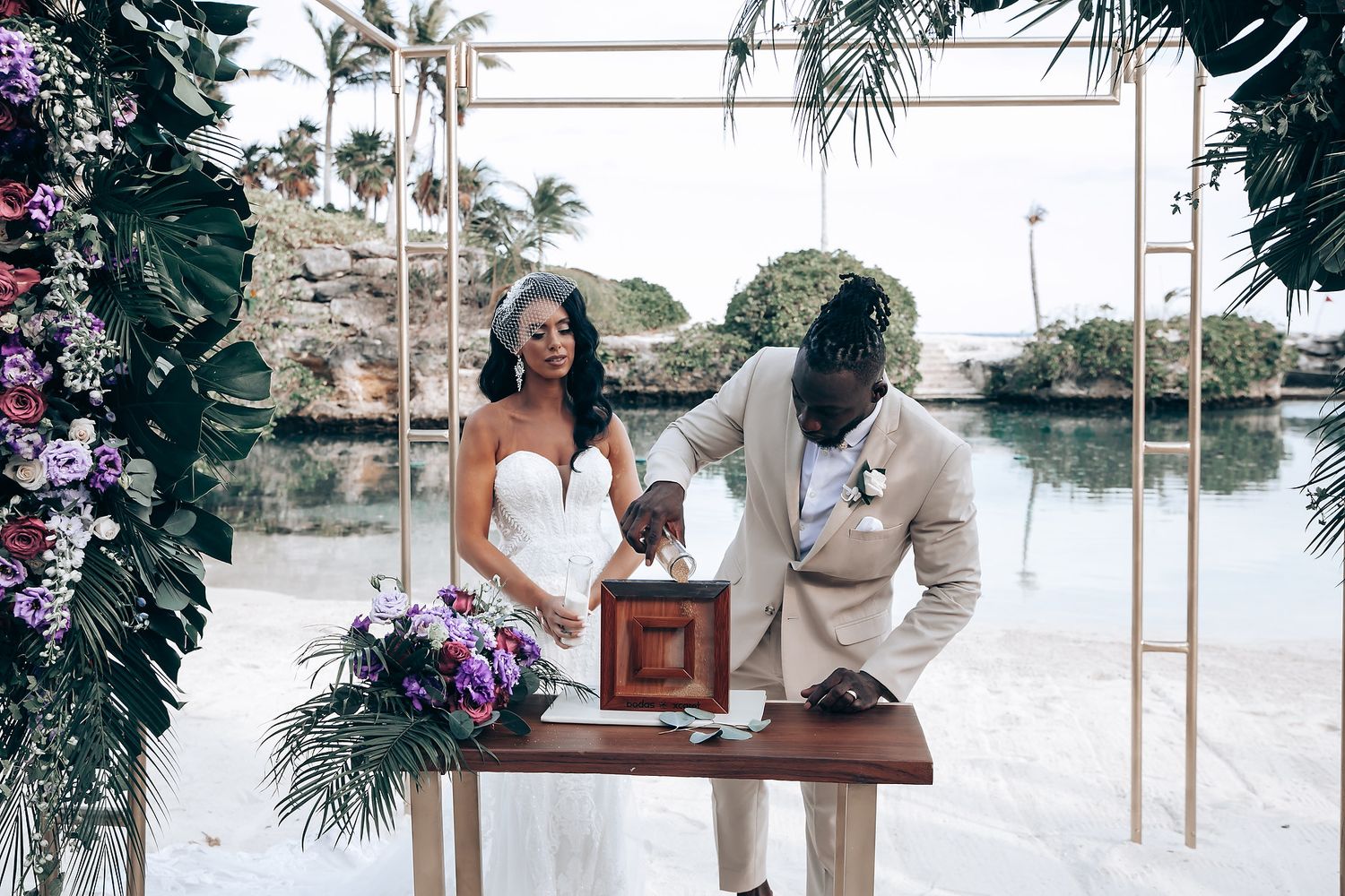Couple signing documents at a wooden table during their beach wedding ceremony.