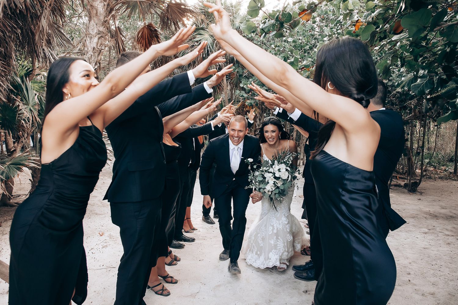 Wedding guests creating a celebratory arch with raised arms as newlyweds walk beneath.