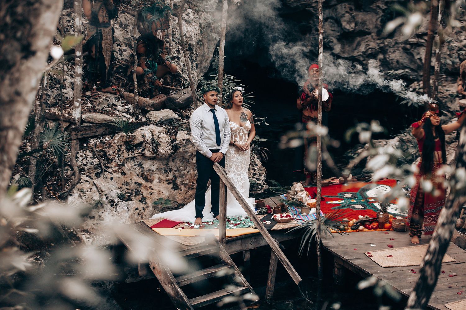 A wedding celebration takes place on a wooden platform surrounded by natural rock formations.