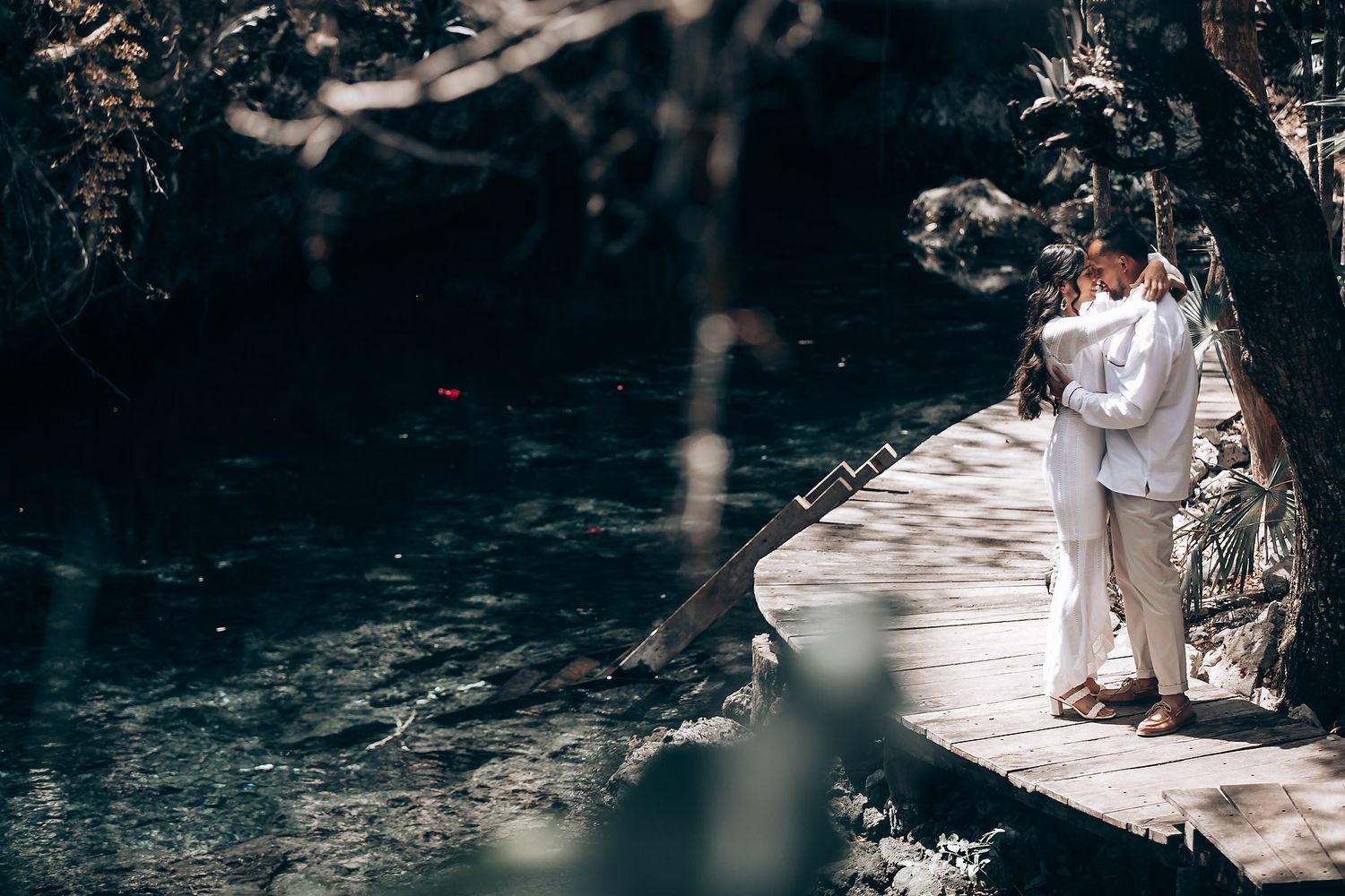 Artistic forest photography with white-dressed figures near water in dark atmospheric lighting.