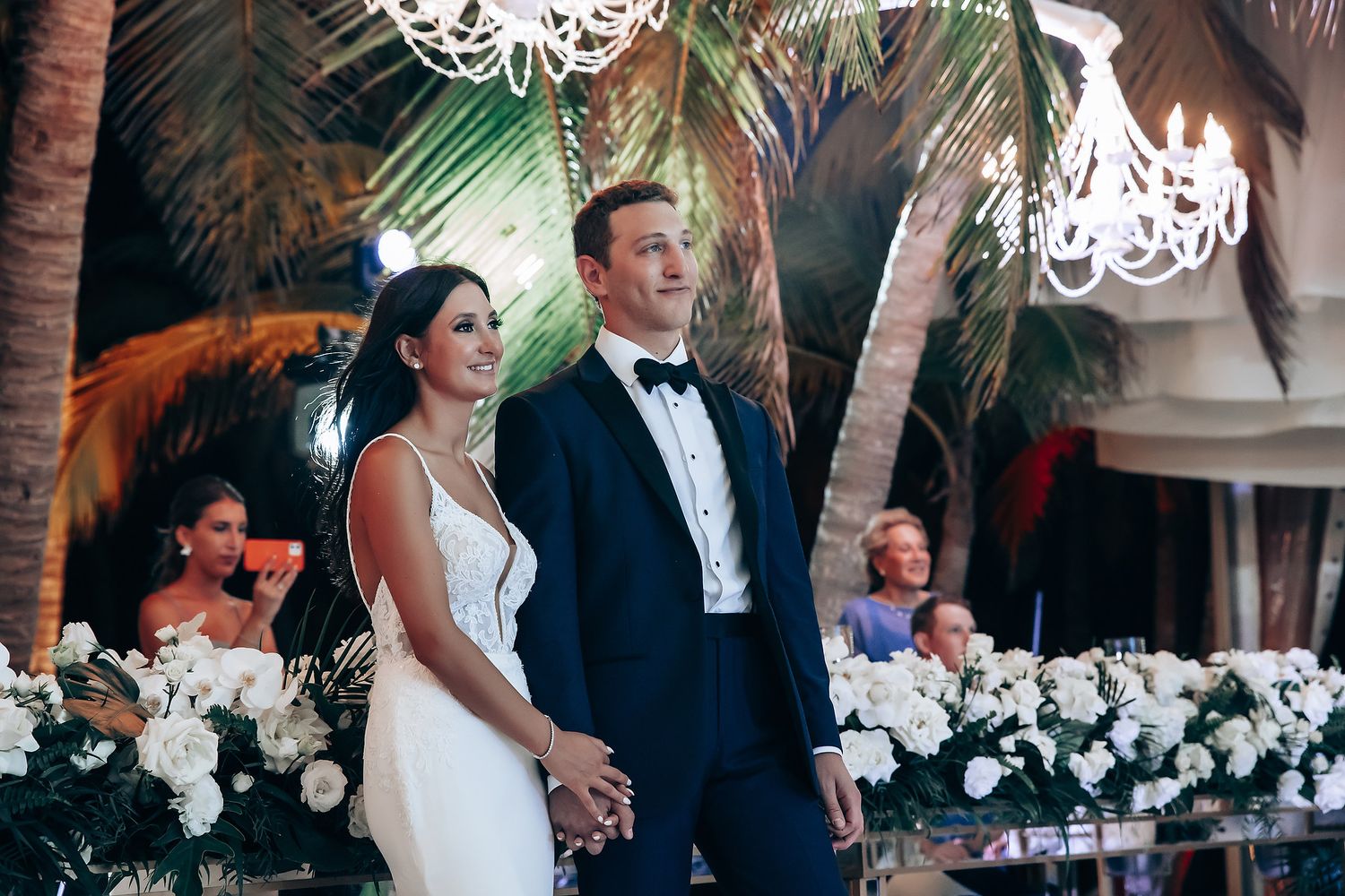 Elegant tropical wedding reception with white floral arrangements and palm trees.