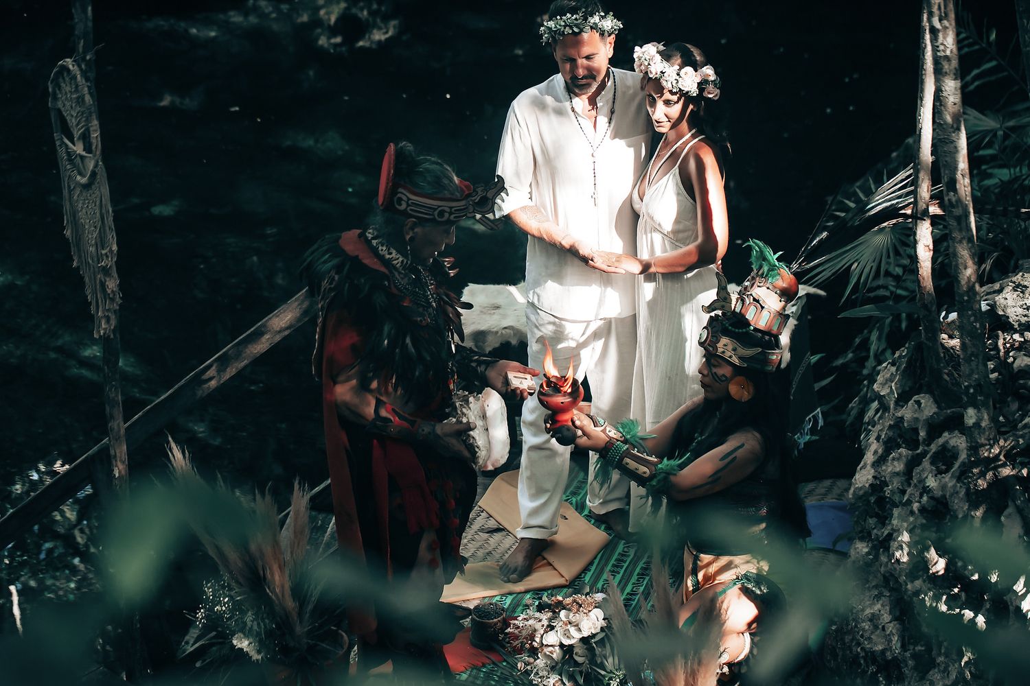 A couple in white clothing stands in a lush, forested setting surrounded by nature.