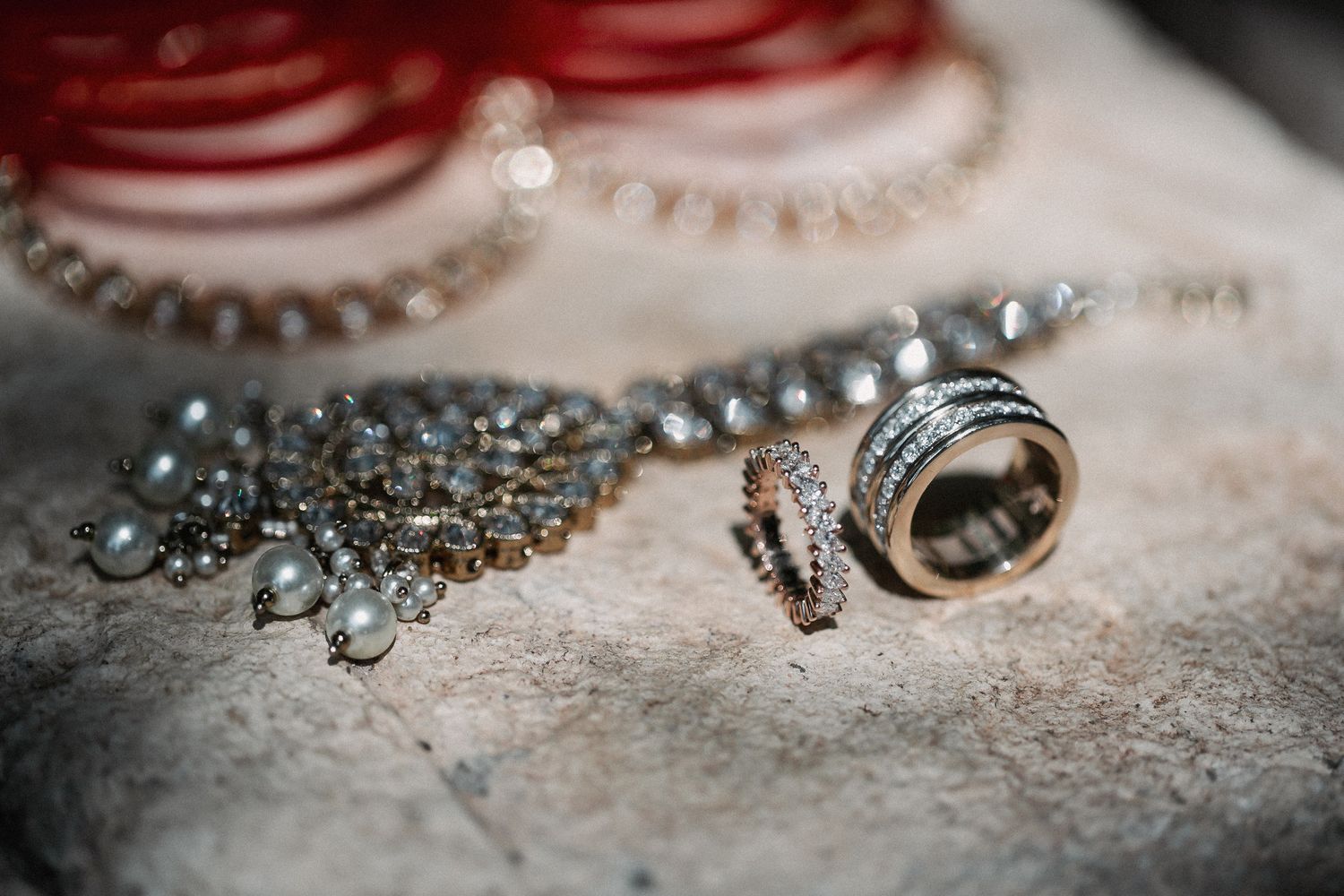 Close-up of elegant jewelry including pearl necklaces, diamond rings, and gold bangles arranged on a stone surface.