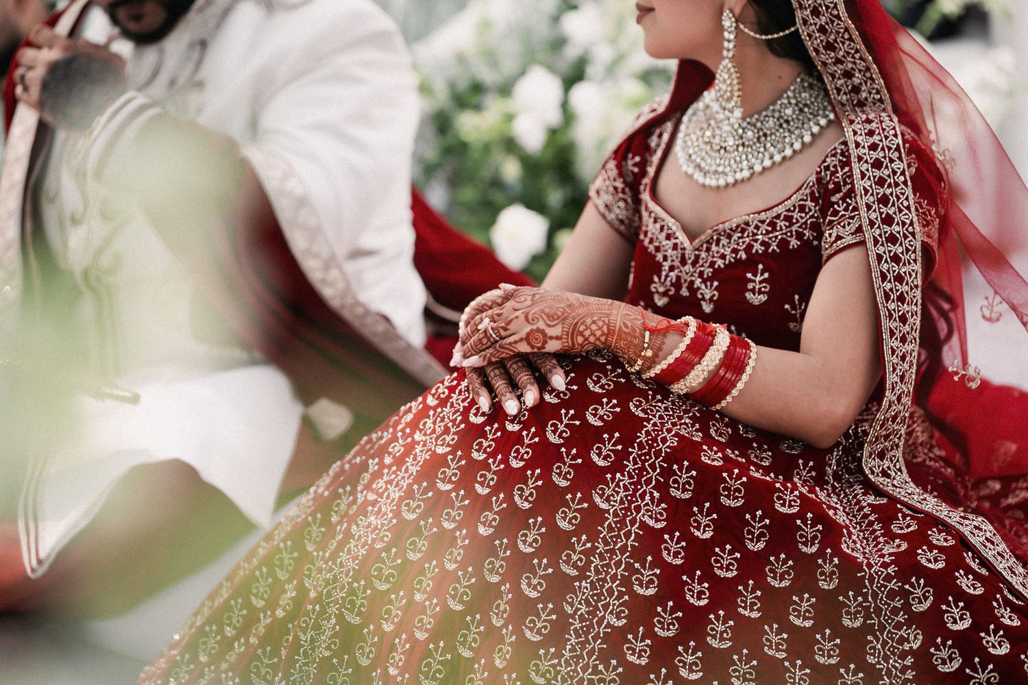Indian bride in ornate red and gold lehenga with intricate embroidery and traditional bridal jewelry at her wedding.