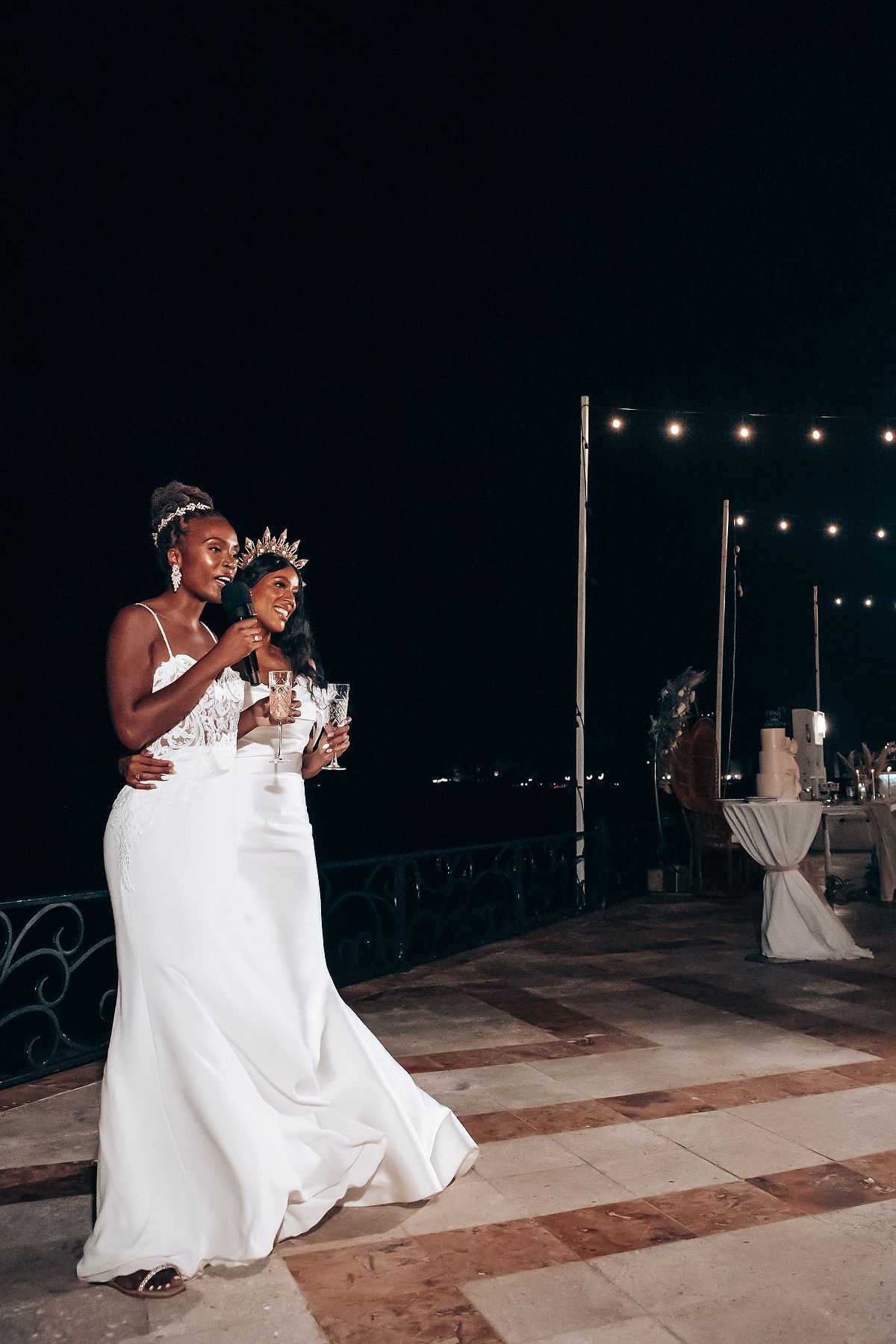 Evening wedding reception dance on waterfront terrace with string lights.