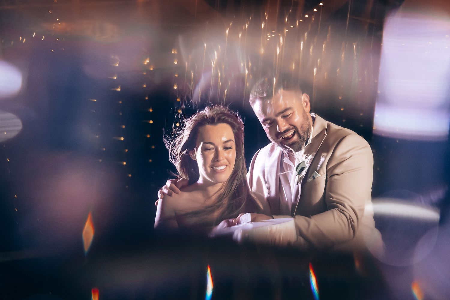 Couple leans close together while working at white desk with twinkling lights in dark setting.