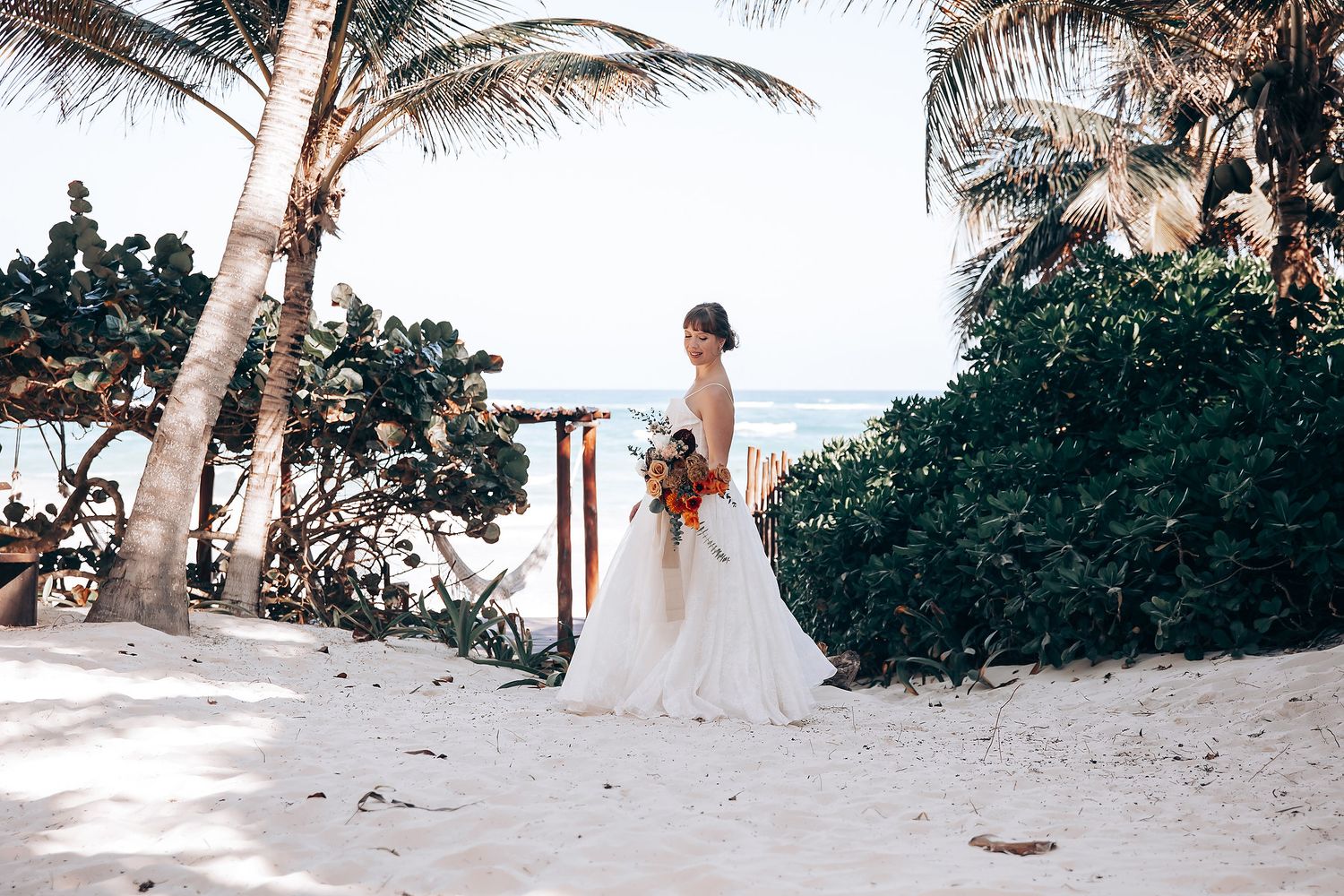A beautiful beachfront wedding ceremony setup with palm trees and white decor along a tropical shoreline.