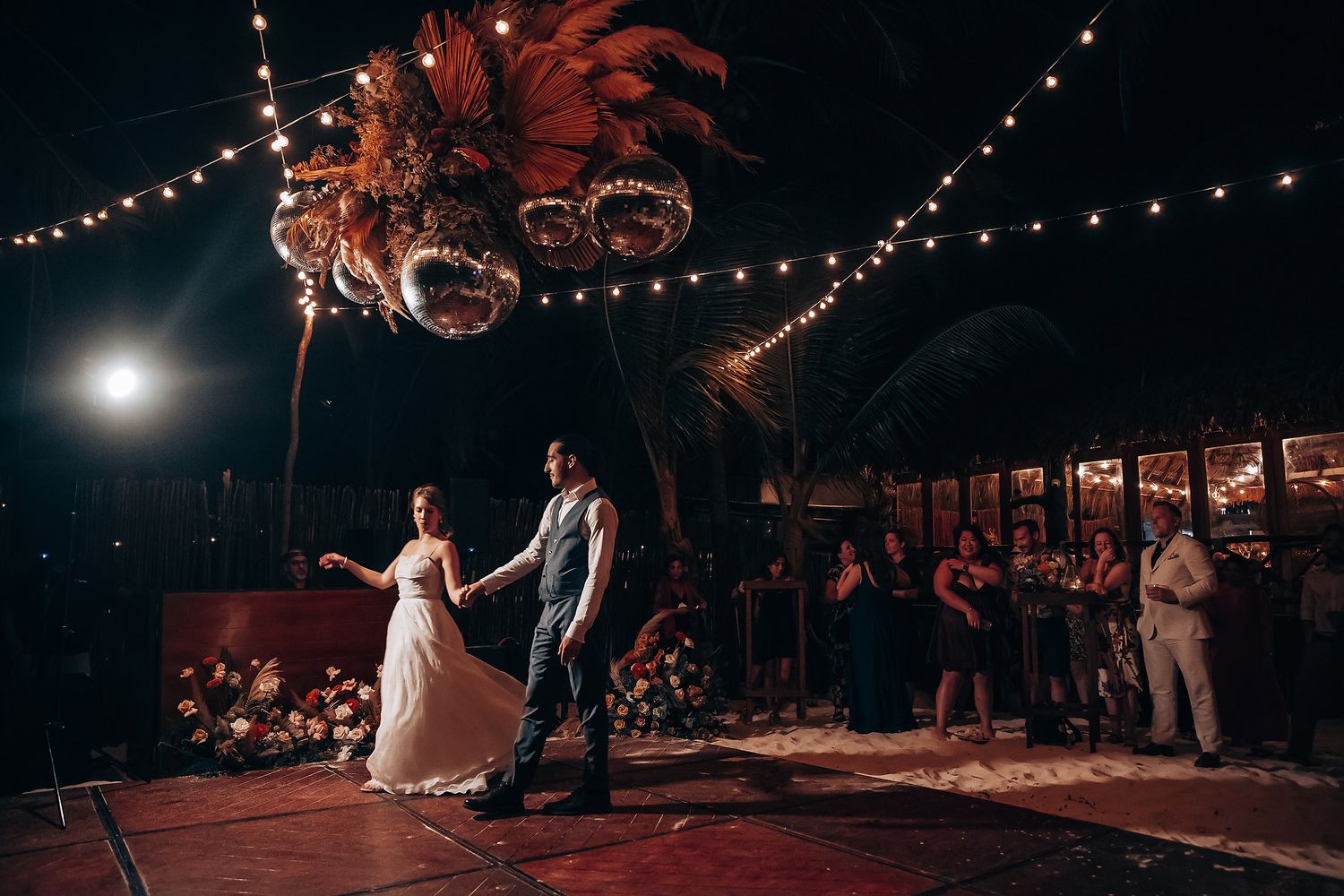 Wedding reception dance floor illuminated by warm string lights and disco ball reflections at an evening celebration.