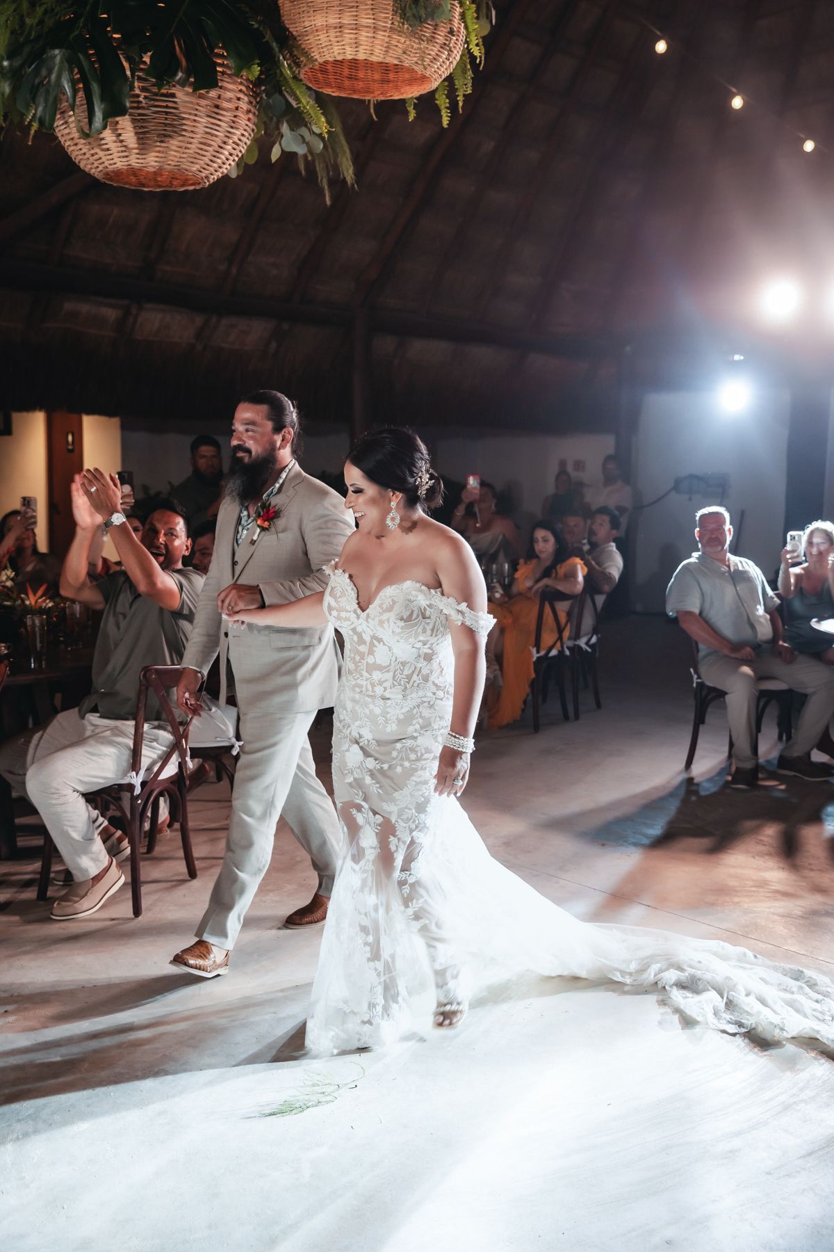 Bride in lace mermaid gown and groom in tan suit share first dance at tropical wedding reception.