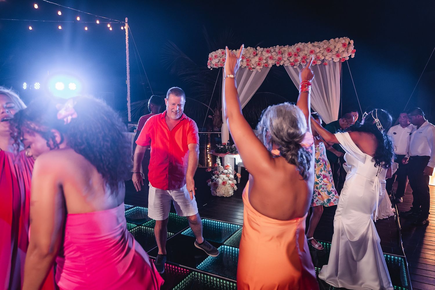 Wedding reception dance floor with string lights and guests celebrating at night.