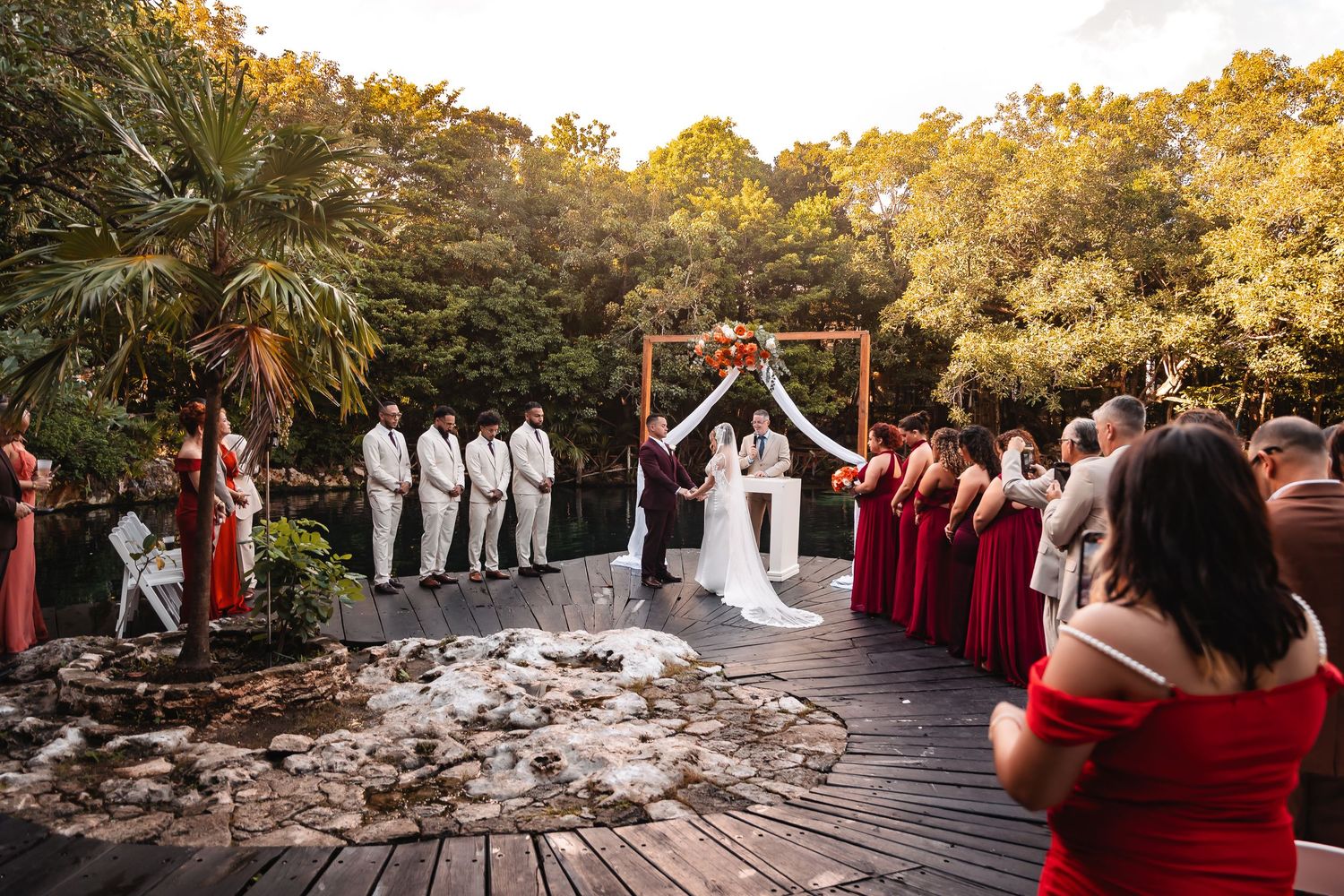 Wide angle shot of wedding ceremony on elevated wooden deck surrounded by lush greenery.