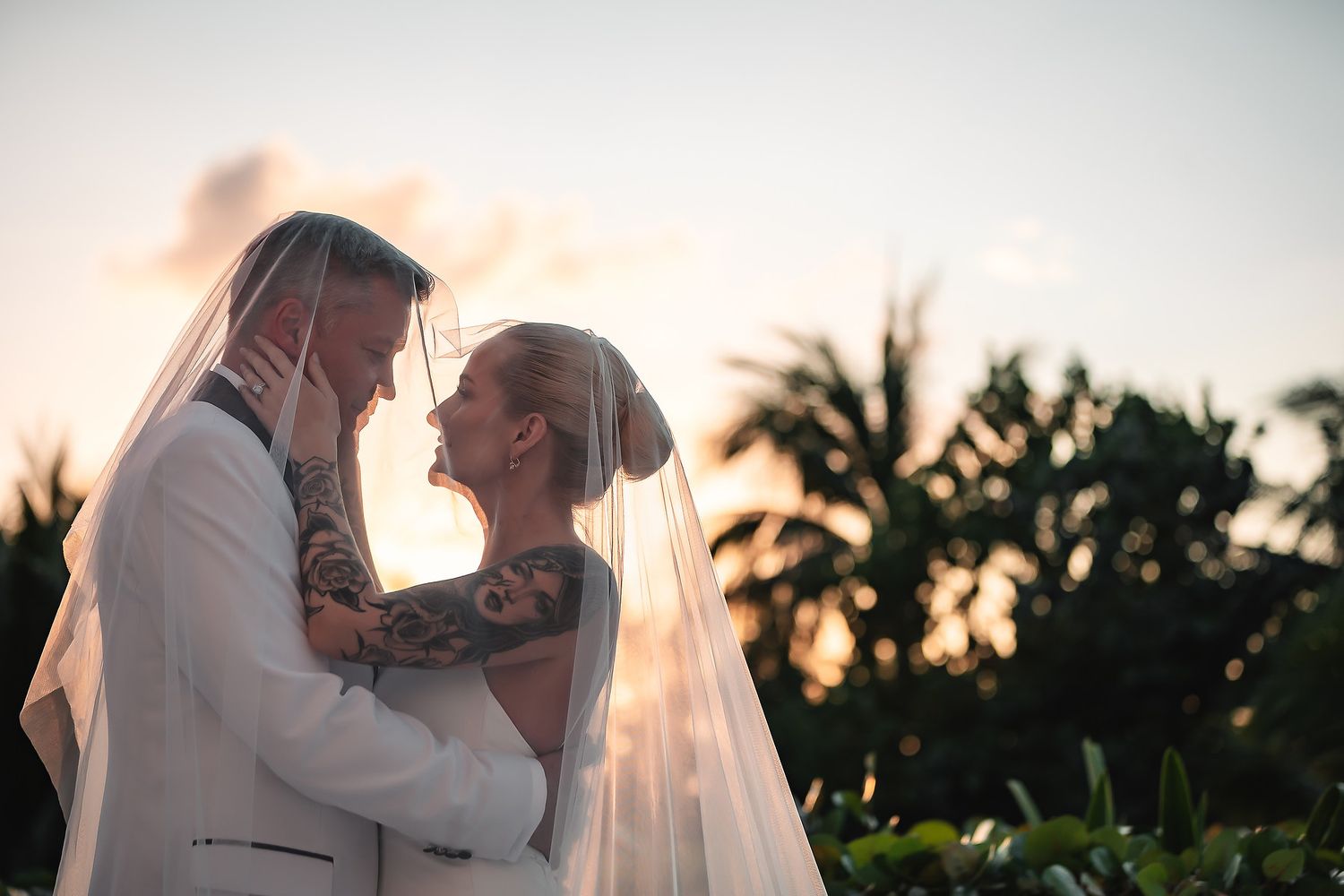 Sunset wedding portrait with palm trees creating a romantic silhouette against the sky.