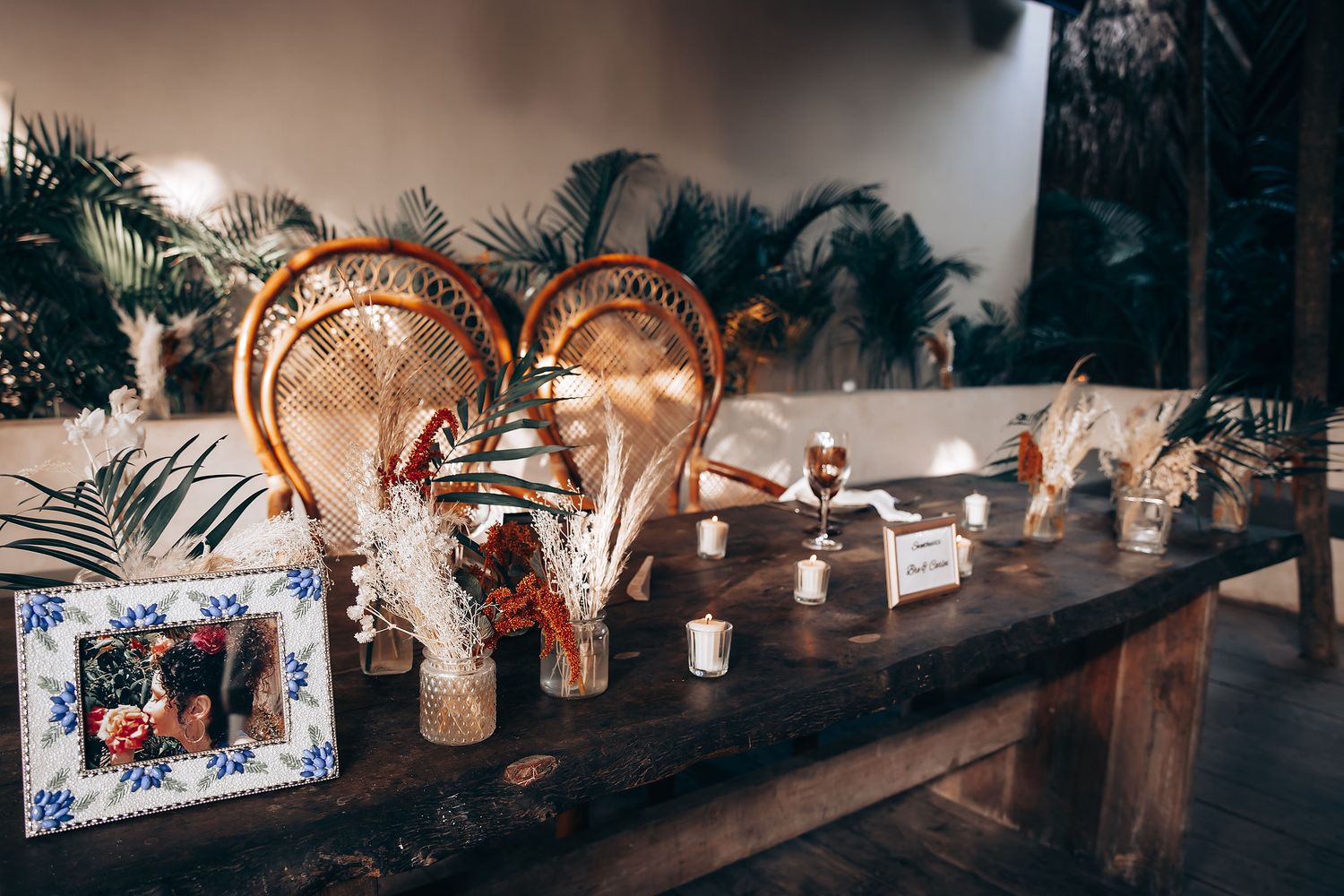 Rustic wooden tables decorated with dried pampas grass and amber glassware create an elegant dining setup.