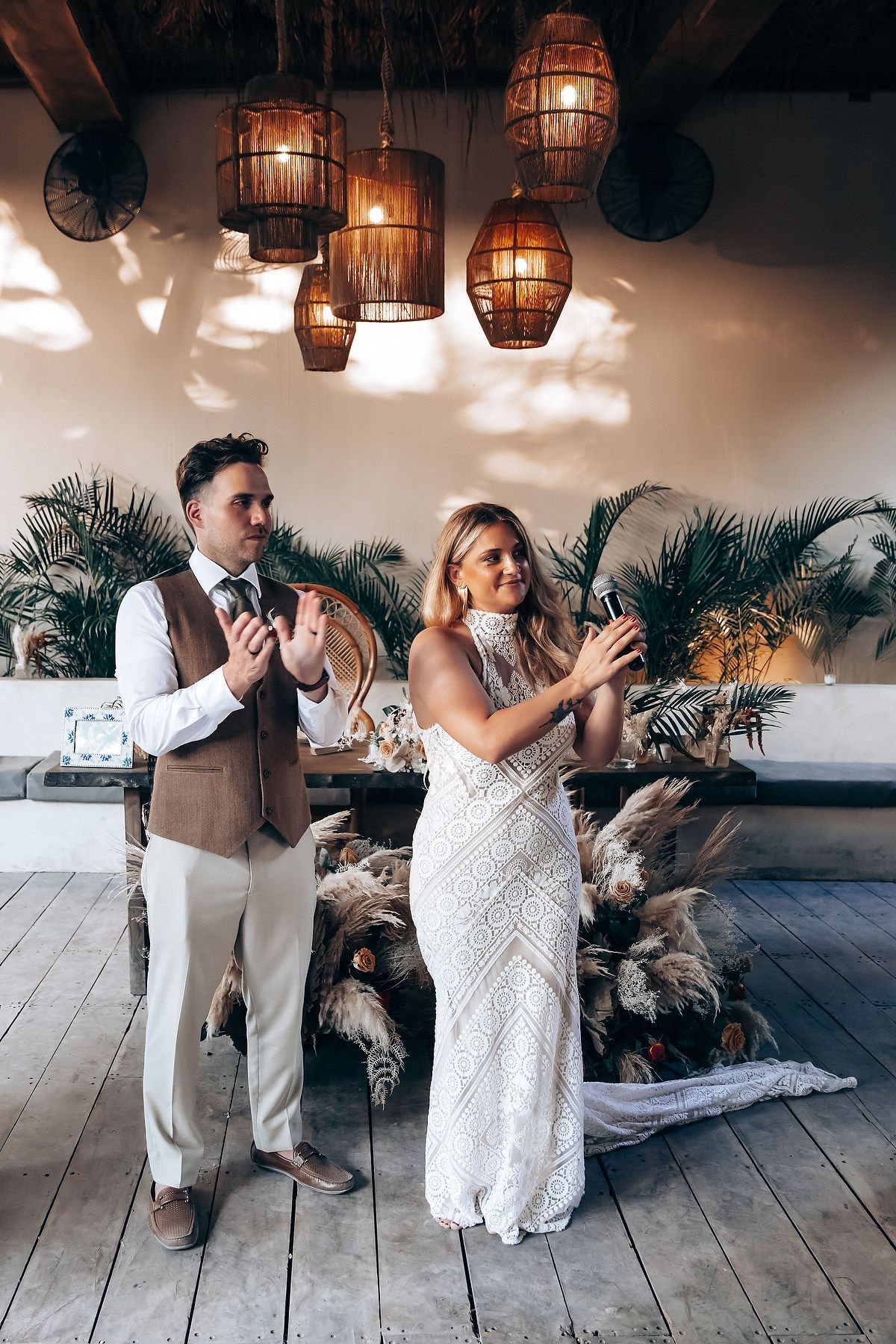 A couple dances together on a rustic wooden floor under hanging wicker lanterns and tropical decor.