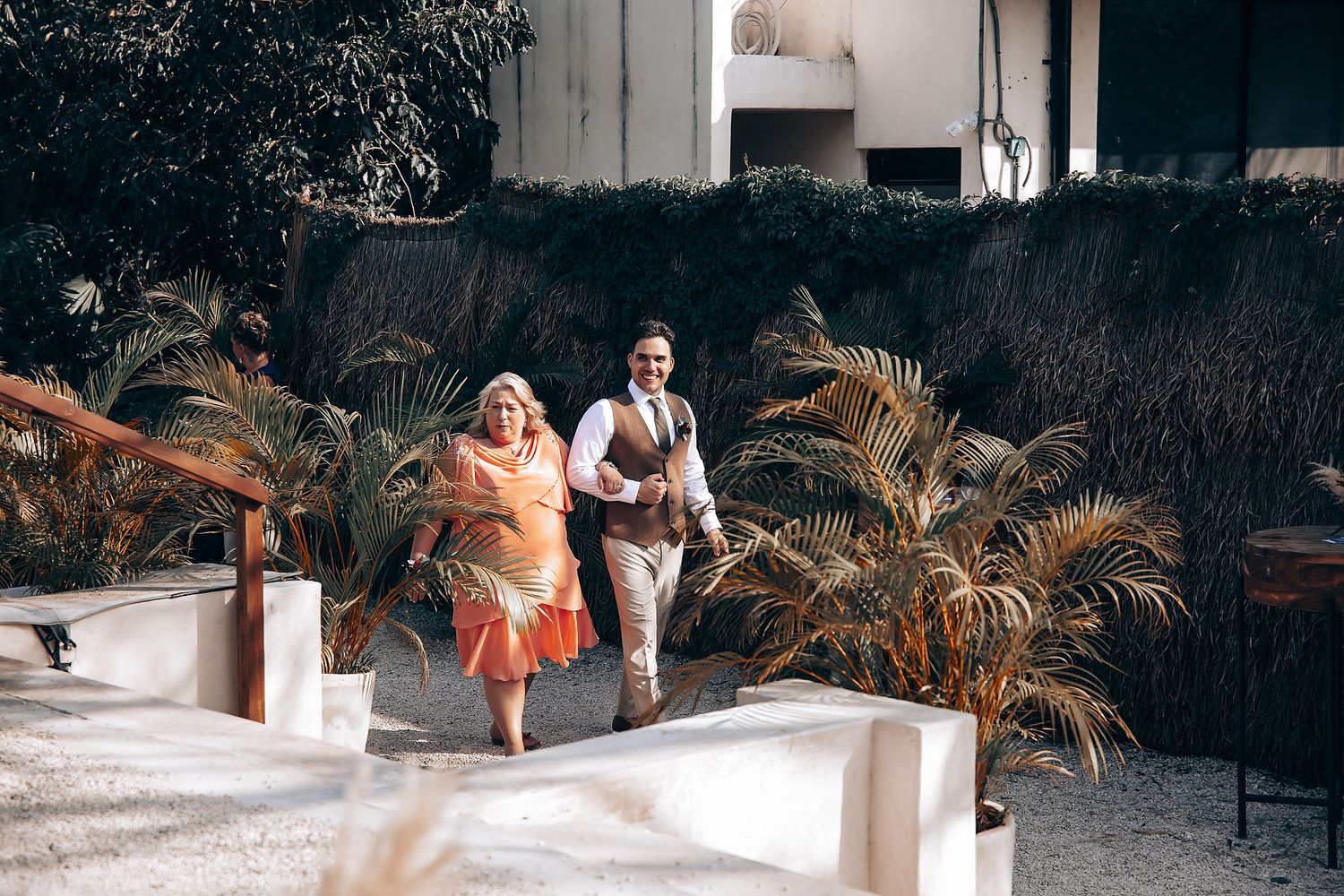 A couple dances and poses together in a tropical garden setting with palm trees and white architecture.