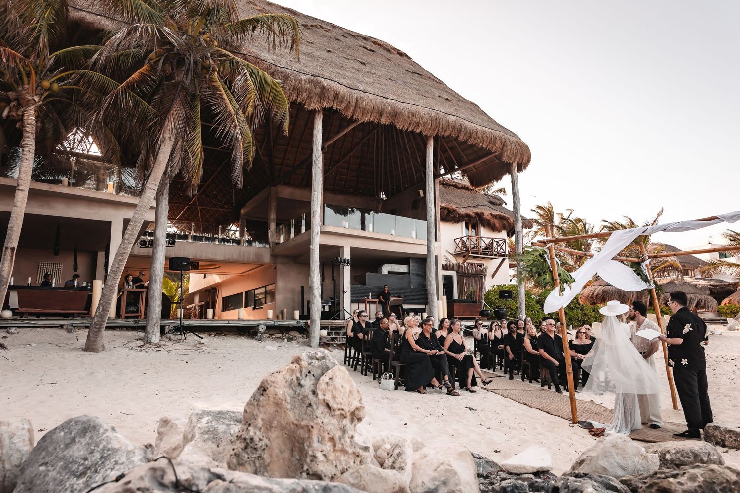 Beachfront wedding venue setup with thatched roof structures and palm trees.