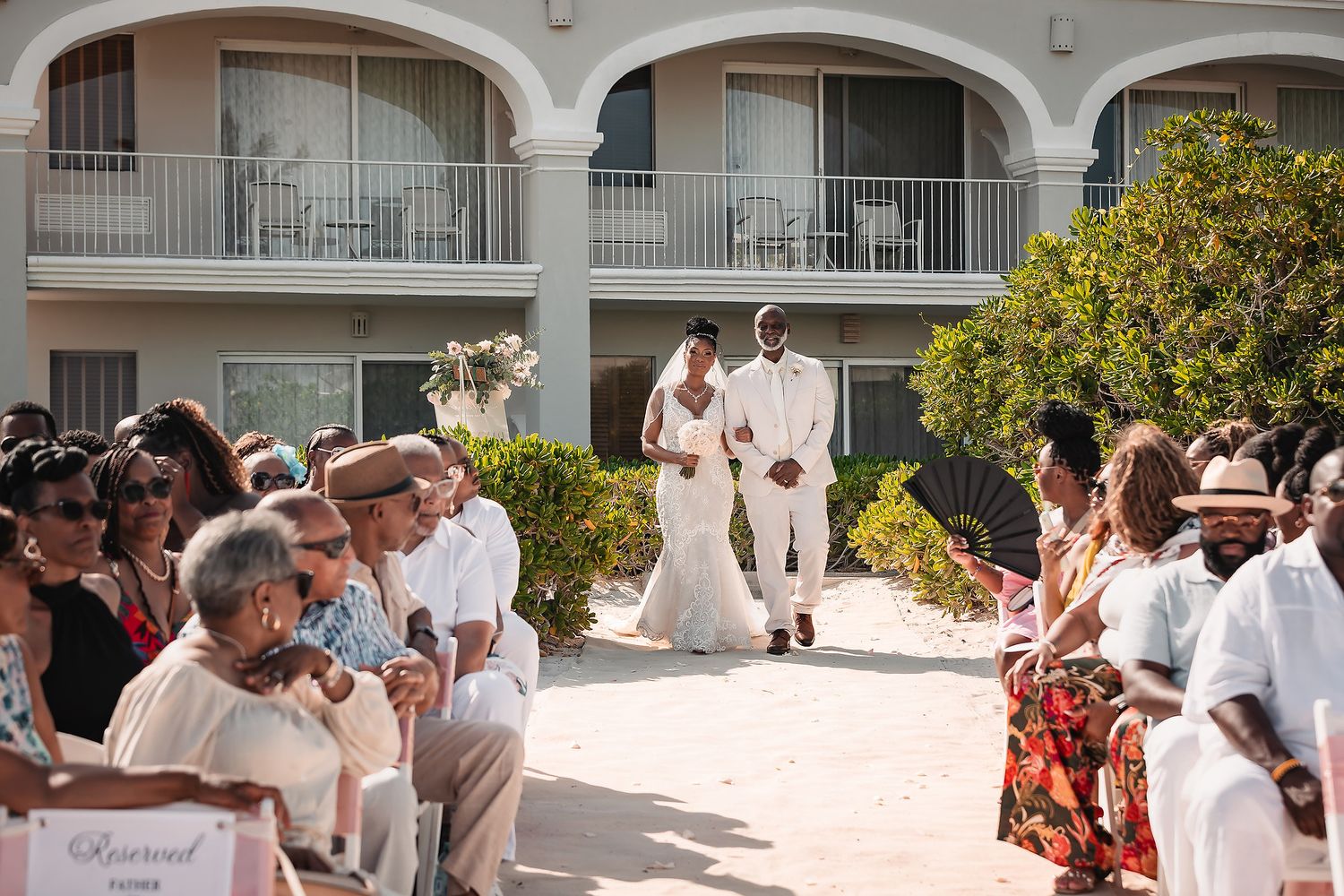 Wedding guests mingling under white arched columns at an outdoor venue.