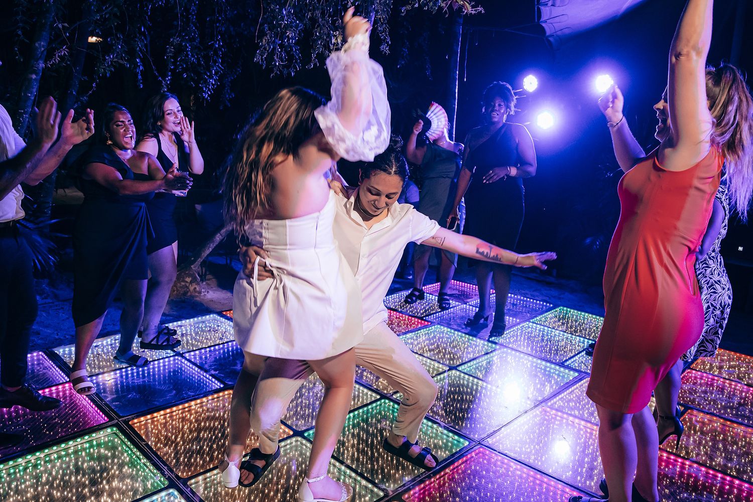 People dancing and enjoying themselves at a nightclub with purple lighting and an illuminated dance floor.