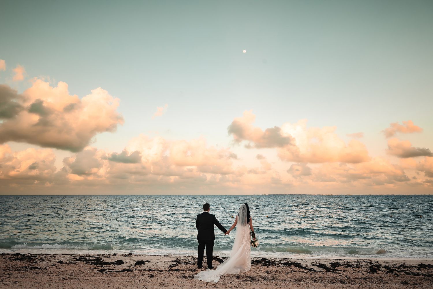 Beach wedding ceremony setup with palm trees and ocean views at sunset.