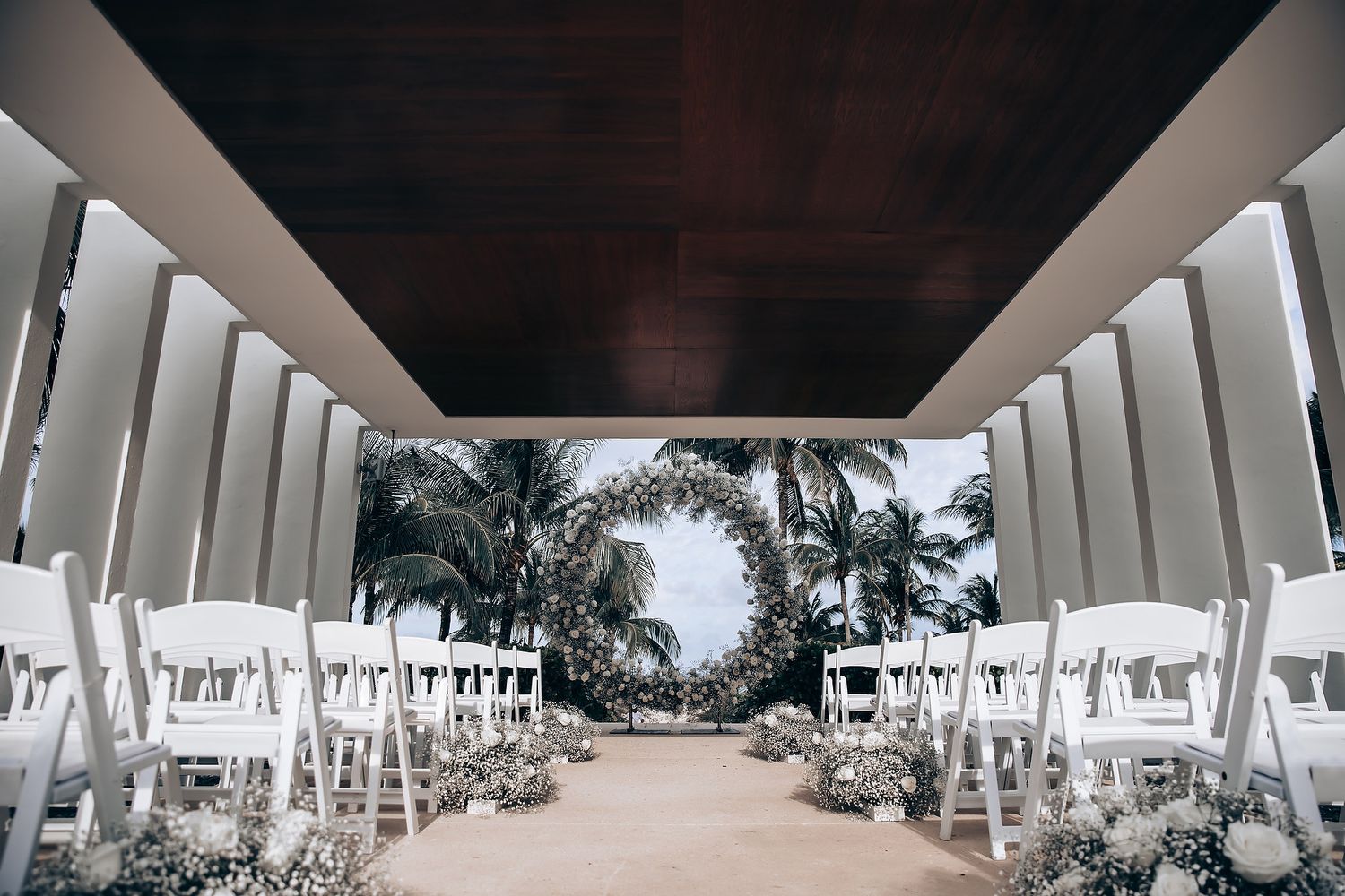Wedding party walking under modern white architectural columns with tropical landscaping.