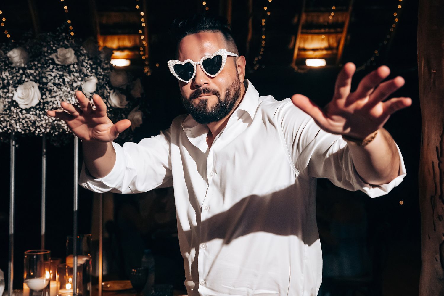Man in white shirt and sunglasses throwing confetti at indoor celebration.