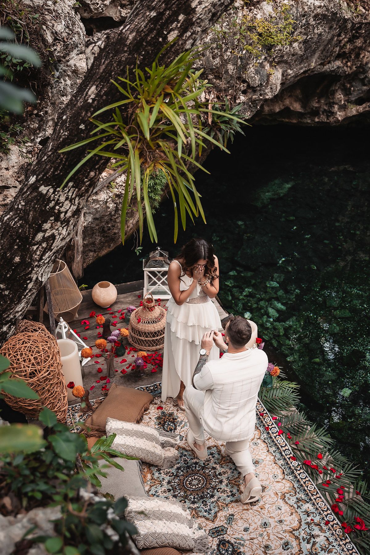 Overhead view of romantic proposal setup on decorated platform near water with lanterns and flowers.