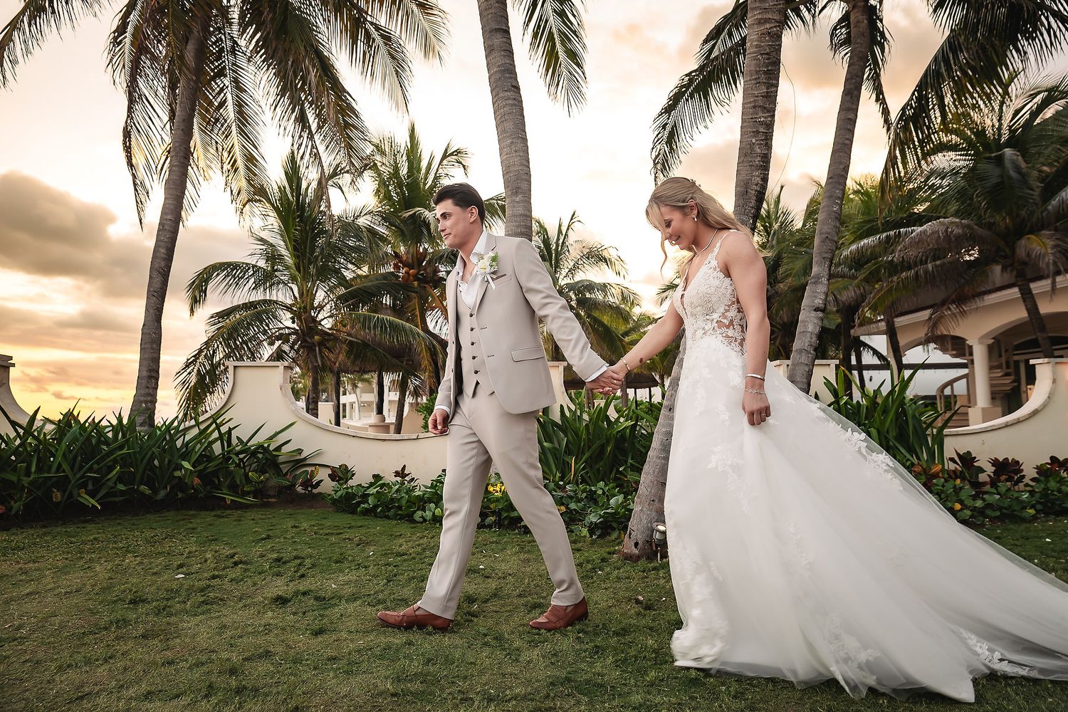 Newlyweds walking along a palm-lined beach at sunset.
