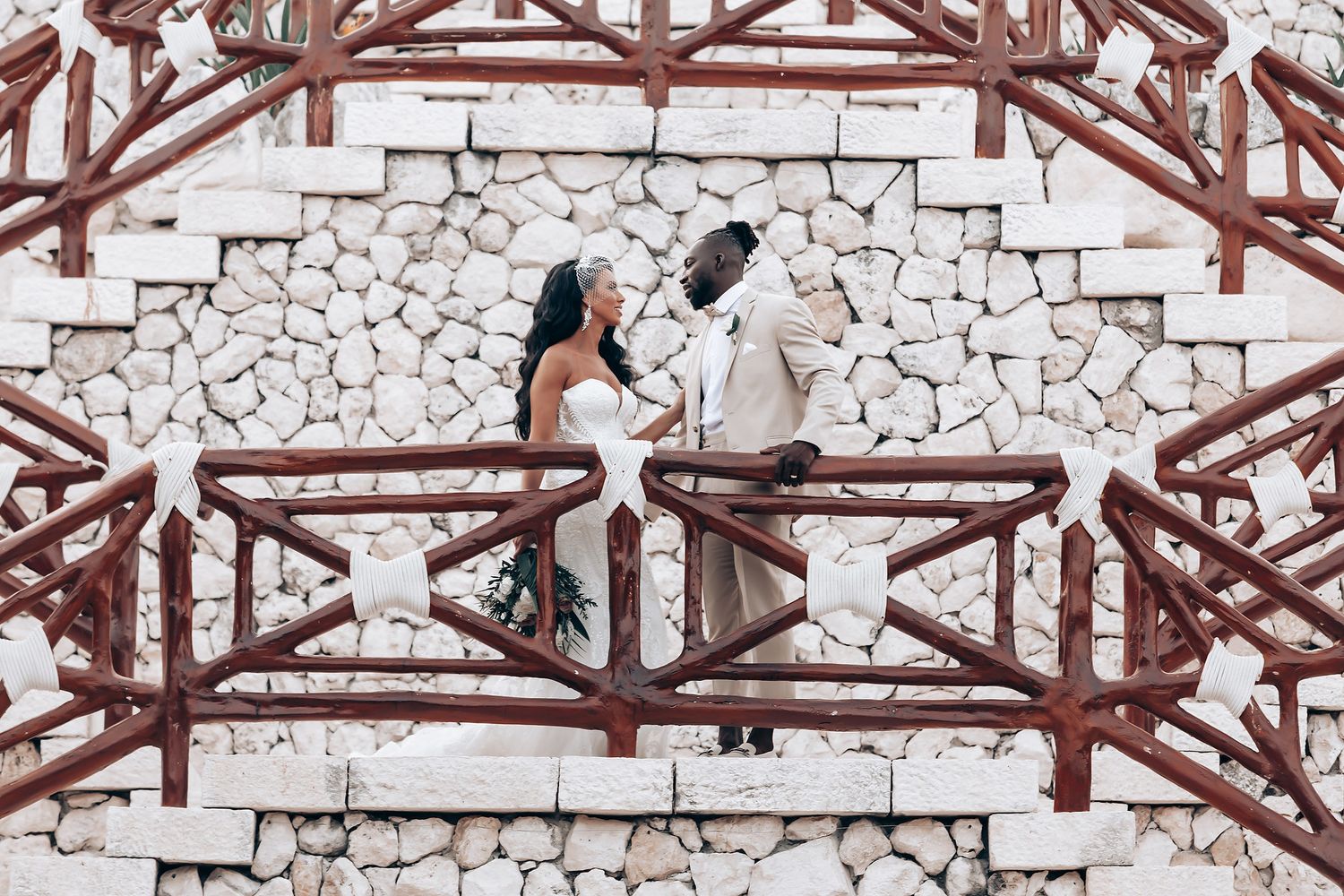 White stone wall with wooden beams creates a rustic architectural backdrop at a tropical venue.
