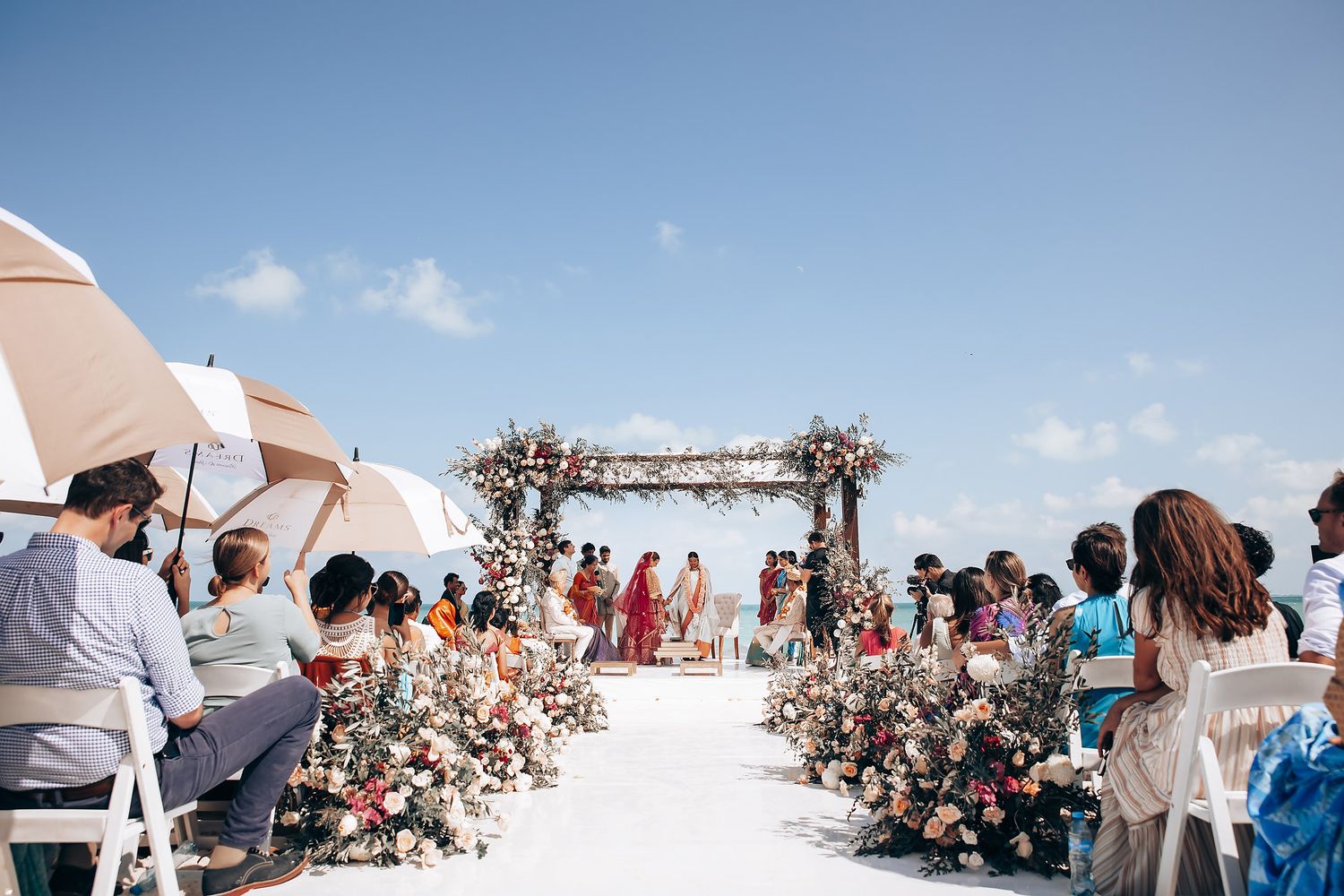 Wide angle view of beach wedding ceremony with guests seated under white canopy.