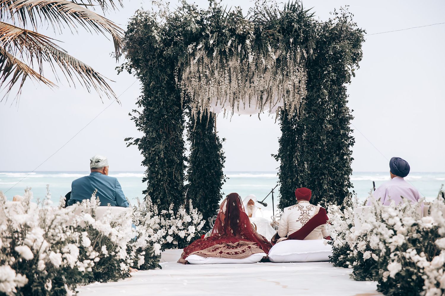 Tropical beach wedding setup with white floral arrangements and palm trees.