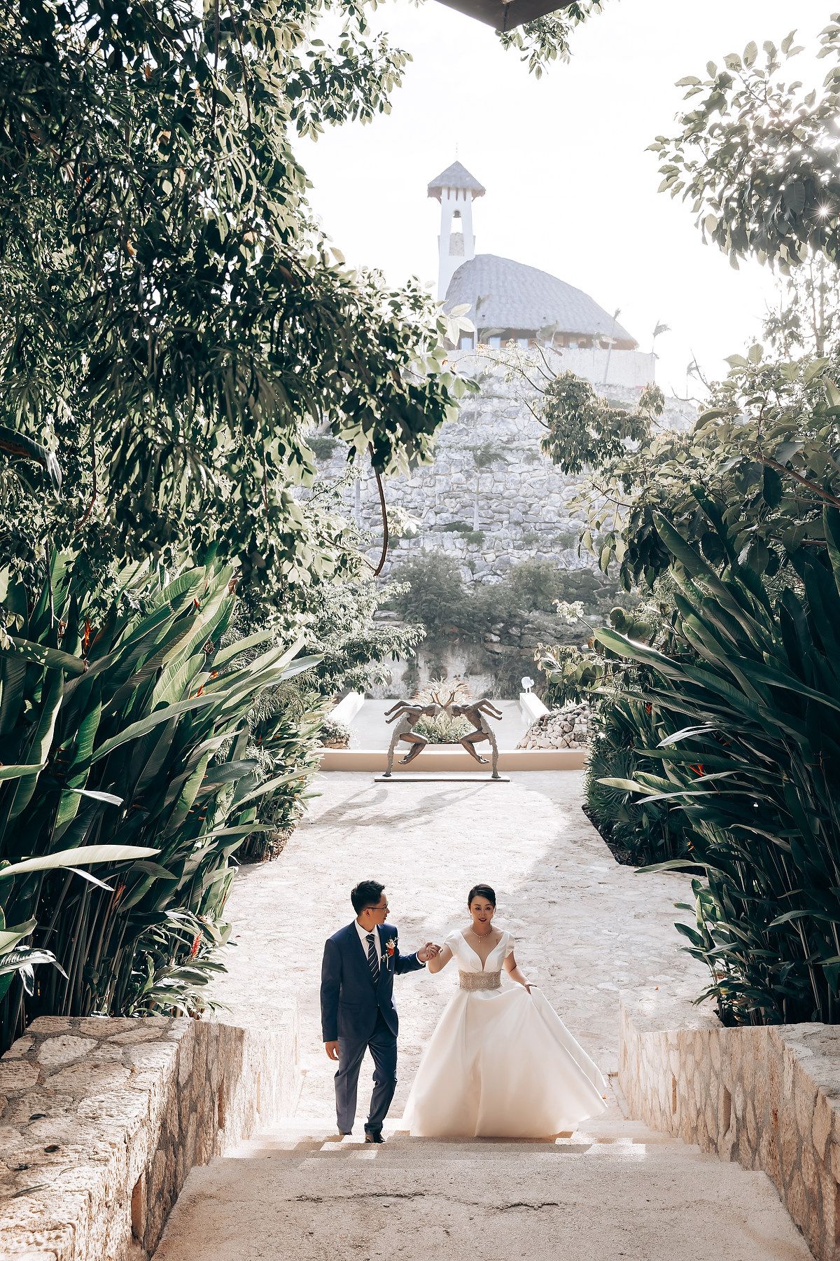 Garden pathway lined with lush tropical plants creates romantic wedding photo setting.
