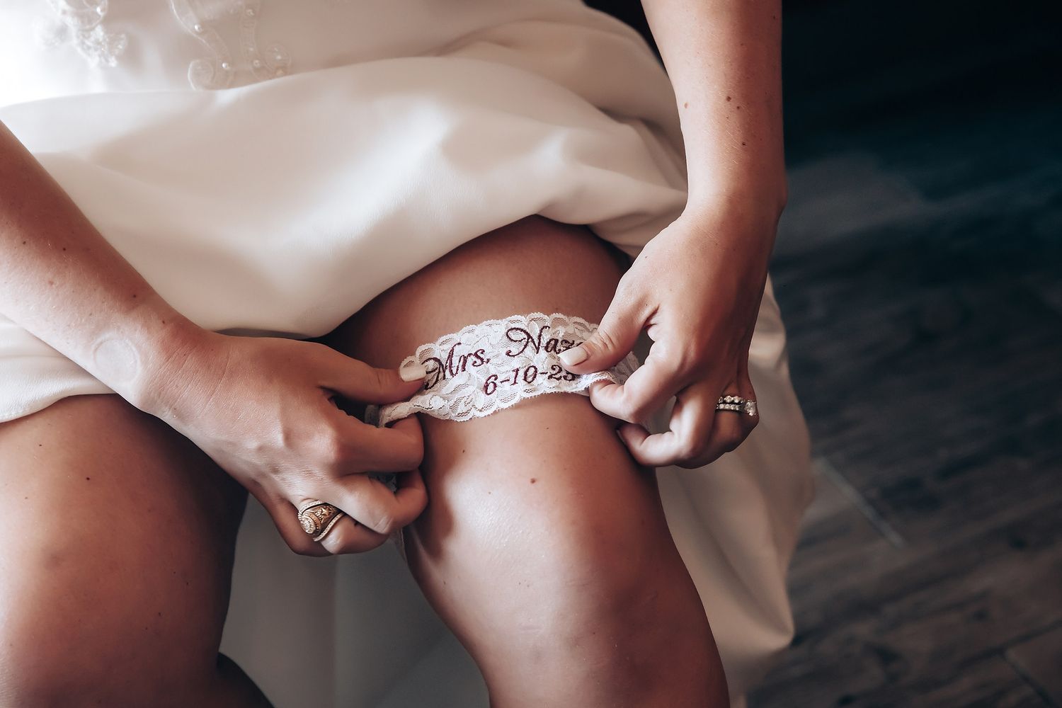 Close-up of a wedding garter with embroidered text being adjusted on leg.