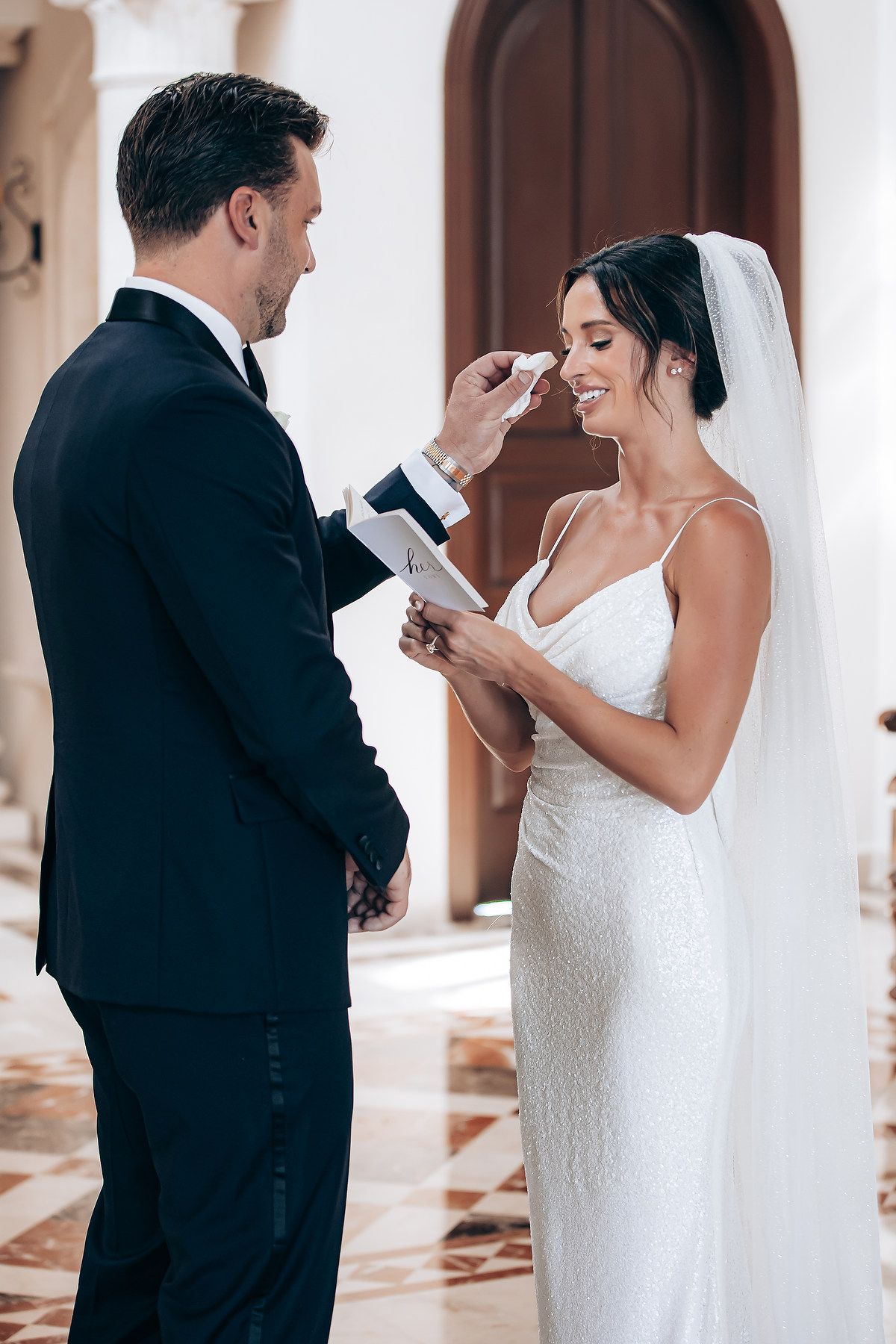Couple shares intimate first look moment in white columned venue hallway.