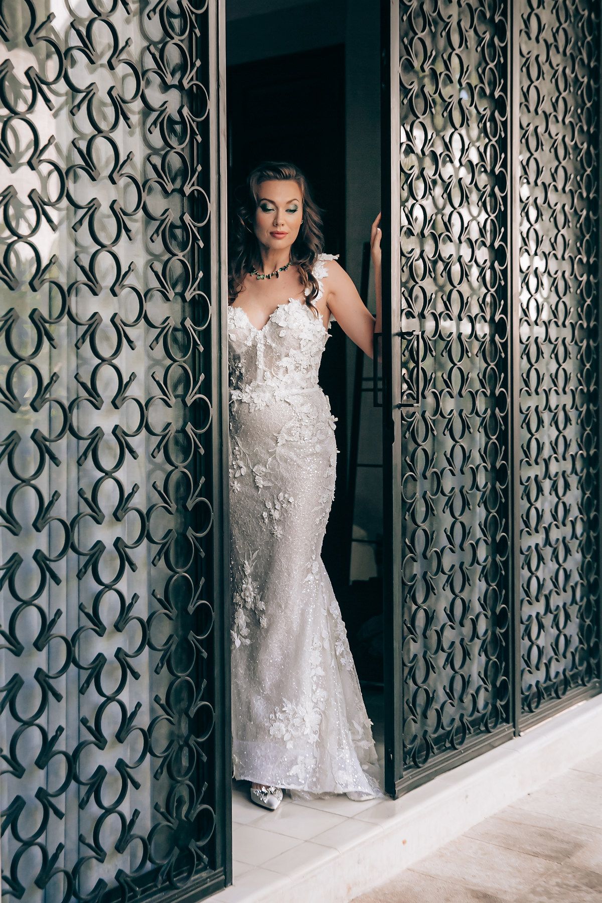 A bride in a lace wedding gown poses against decorative iron doors.