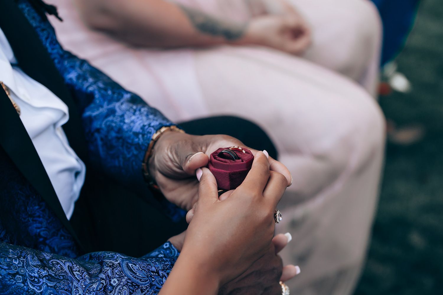 Close-up of hands holding a small burgundy ring box during a formal event.