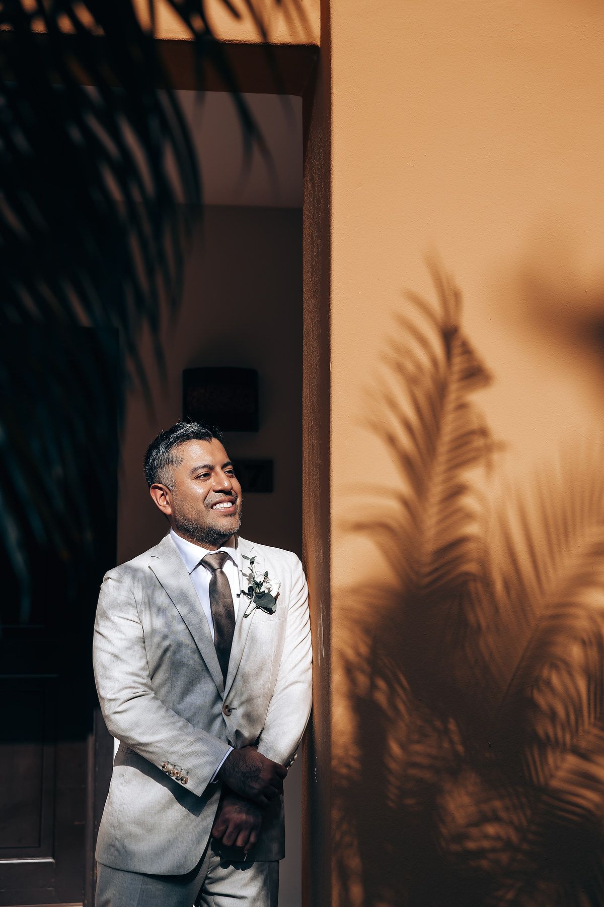 A series of candid photos showing someone in a white suit jacket laughing and smiling against a shadowy palm leaf backdrop.