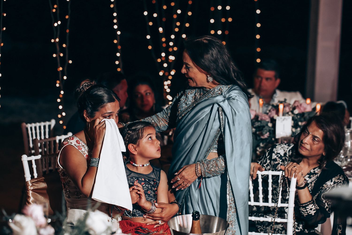 Reception venue decorated with string lights and white chairs as guests mingle during evening celebration.
