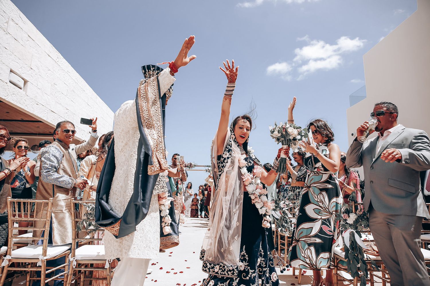 Wedding celebration with guests throwing confetti and raising hands in celebration outside white building.