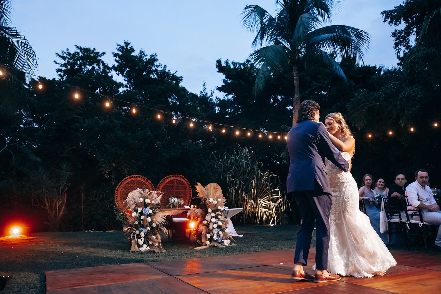 Evening wedding reception with string lights creating a magical atmosphere under palm trees.