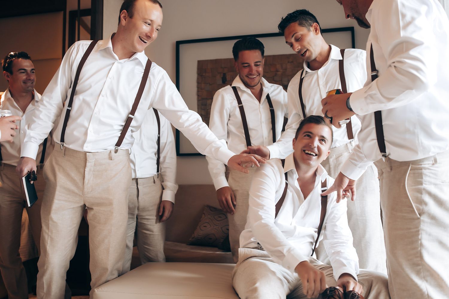 A group wearing white shirts and suspenders share a candid laughing moment together.