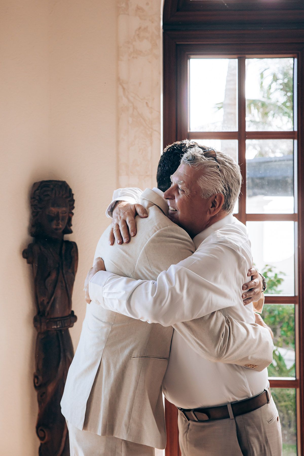 Two people in white clothing embrace in a sequence of emotional reunion photos by a window.