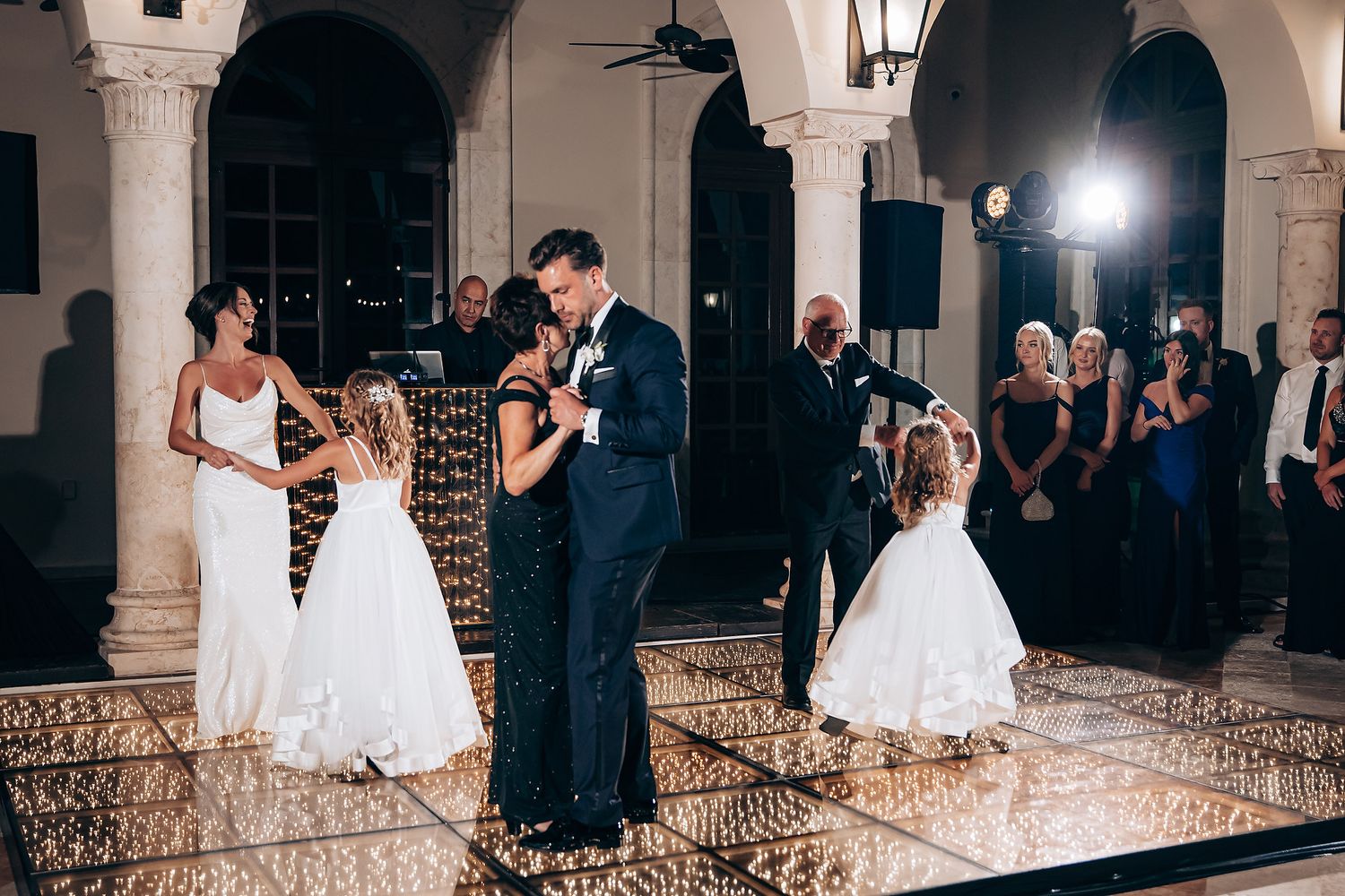A couple shares their first dance at an elegant wedding reception under arched columns and romantic lighting.