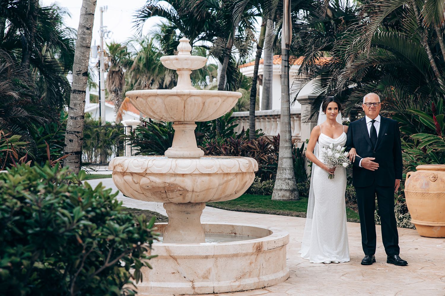 Outdoor wedding ceremony setup with stone fountain and tropical palm trees creating an elegant backdrop.