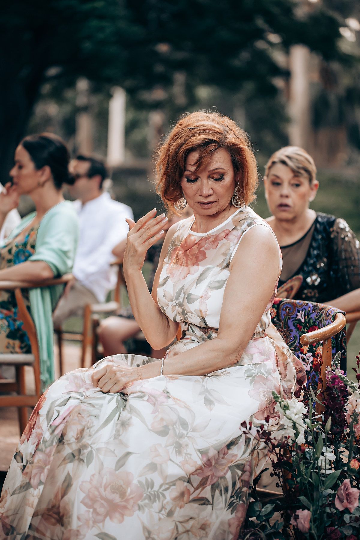 A bride in a white dress laughs joyfully while sitting outdoors during a wedding celebration.