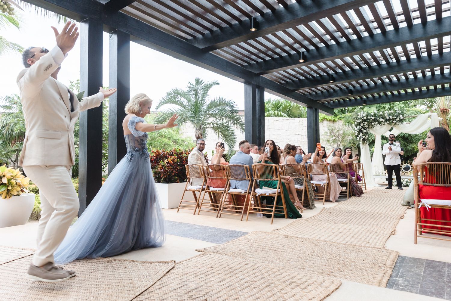 Bride in blue tulle gown and groom celebrate their grand entrance at an outdoor wedding reception under a pergola.
