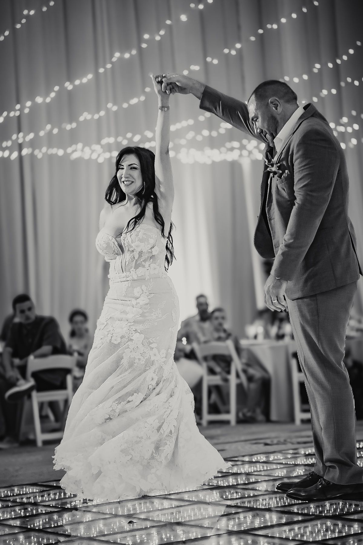 Black and white photo of bride and groom sharing first dance, groom spinning bride on mirrored dance floor.
