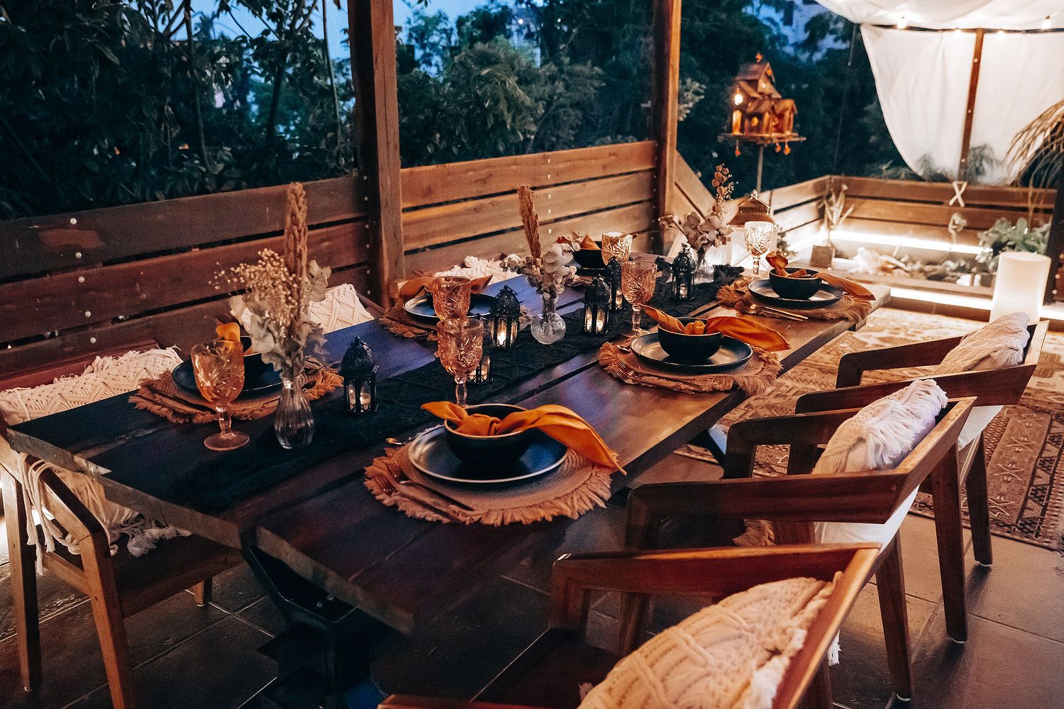 Bohemian outdoor wedding tablescape with black plates, woven placemats, and warm candlelight at dusk.